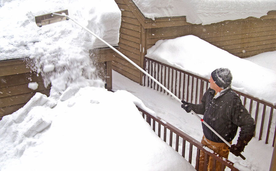 man using roof rake to remove roof snow on a garage